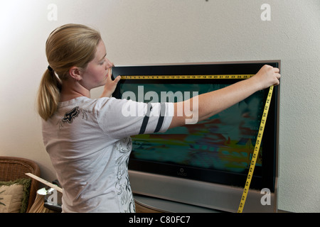 Ragazza adolescente misure le dimensioni di una TV 32 pollici schermo. Signor © Myrleen Pearson Foto Stock