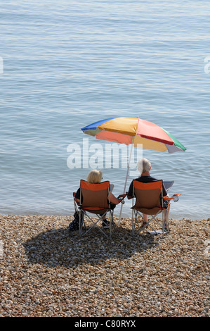 Coppia di anziani a leggere i giornali sulla spiaggia a Lyme Regis Dorset England Regno Unito Foto Stock