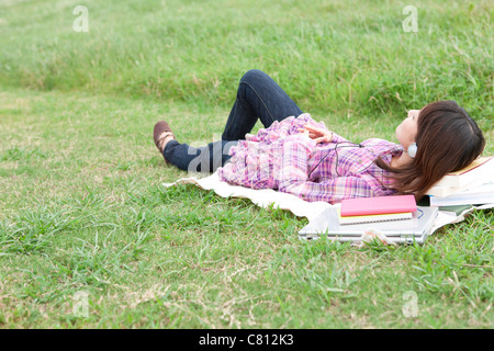Studentessa giacente su erba e ascoltando le cuffie Foto Stock