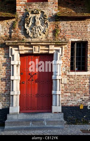 La pesante porta di legno e di pietra scolpita crest del xviii secolo De Pelikaan almshouse lungo il Groenerei a Bruges, Belgio Foto Stock