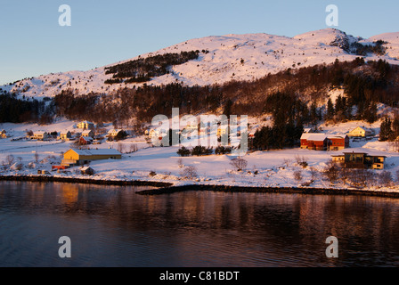 Rosso Giallo e bianco in legno case norvegesi lungo il fiordo con montagne innevate. Foto Stock