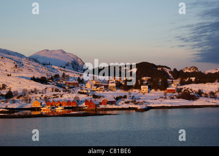 Rosso Giallo e bianco in legno case norvegesi lungo il fiordo con montagne innevate. Foto Stock