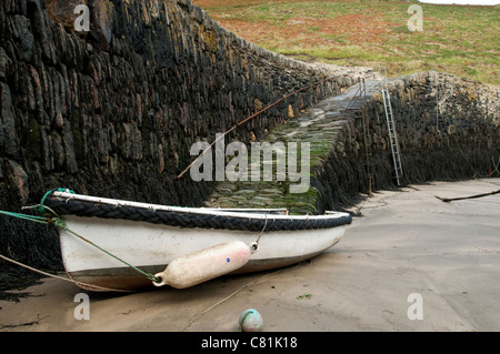 Una piccola barca legato alla parete del porto con la bassa marea. Foto Stock