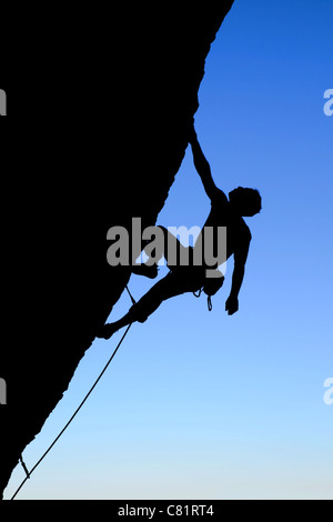 Silhouette di rocciatore salendo una rupe a strapiombo con cielo blu sullo sfondo Foto Stock