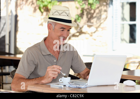 Grigio uomo dai capelli di bere il caffè sulla terrazza con computer portatile Foto Stock