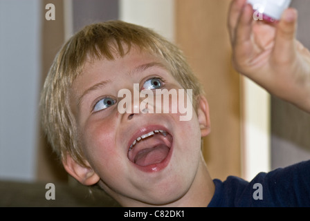 Giovane poco ragazzo biondo vestito con una maglietta blu inclinando la testa cercando intensamente ammirando qualcosa con ampia bocca aperta Foto Stock