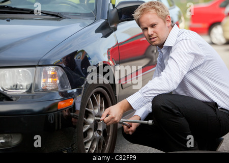 Un infelice business man cambiando un pneumatico su strada Foto Stock