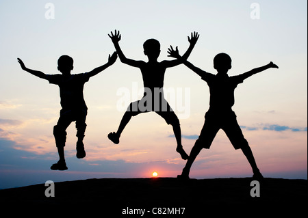 Silhouette di giovani ragazzi indiani jumping contro al tramonto. India Foto Stock