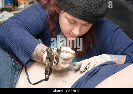 Femmina di ottenere un betty boop tatuaggio sul suo lato inferiore destro mostra tattoo artist in azione Foto Stock