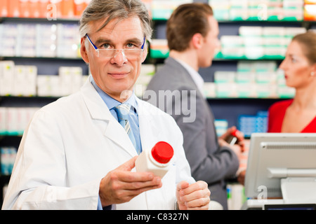 Il farmacista con clienti in farmacia, egli è in possesso di una bottiglia con prodotti farmaceutici in mano Foto Stock