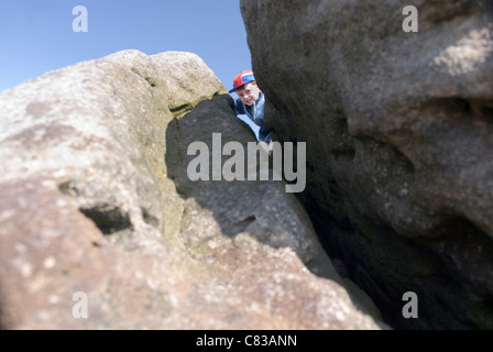 Little Boy Peaking se crepa nel Giant Boulder Rock sulla parte superiore del bordo di macina, nr sorpresa vista, Peak District, REGNO UNITO Foto Stock