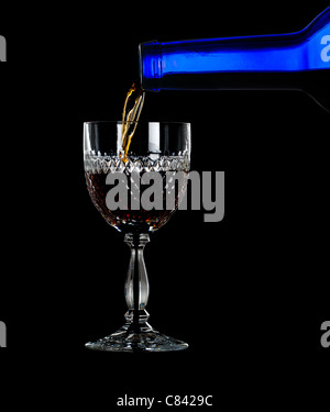 Sherry, la porta o il whisky versata da blu bottiglia di vino in un elegante taglio di vetro e isolata contro il nero Foto Stock