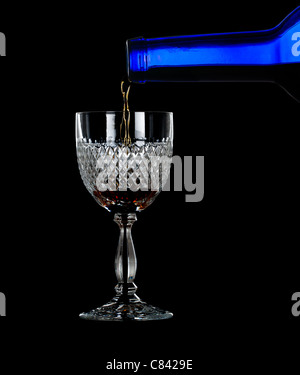 Sherry, la porta o il whisky versata da blu bottiglia di vino in un elegante taglio di vetro e isolata contro il nero Foto Stock