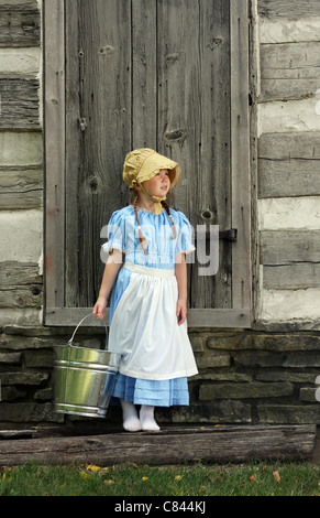 Un bambino con un pallido di mungitura accanto a un log cabin Foto Stock