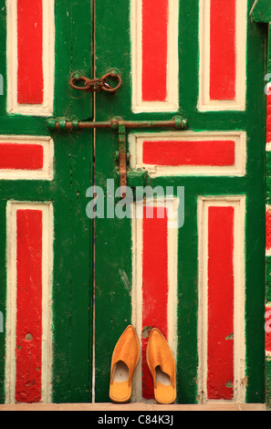 Marocchino tradizionale pantofole/babouches appoggiata contro decorata in tipico legno porta marocchina, medina di Essaouira, Marocco Foto Stock