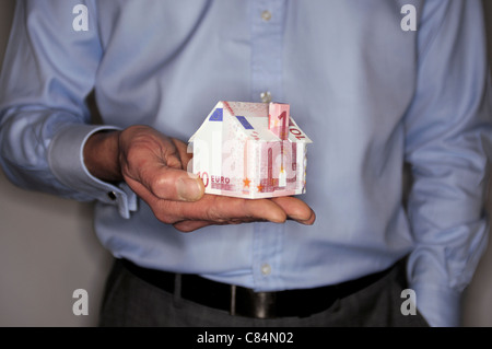 Uomo con modello di casa piegato con banconote in euro, metà sezione Foto Stock