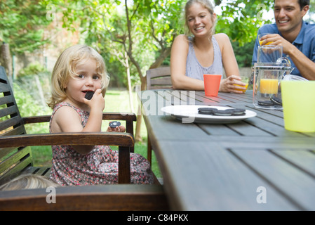 Bambina di mangiare uno spuntino con i suoi genitori all'aperto Foto Stock