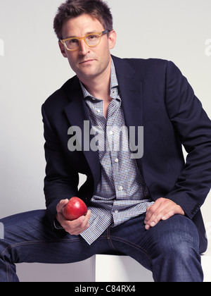 Vestiti alla moda uomo nei suoi anni trenta i jeans e una giacca elegante tenendo un Apple nella sua mano Foto Stock
