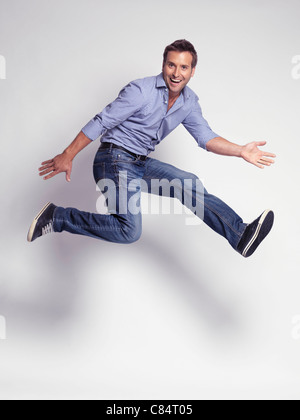 Happy jumping giovane uomo che indossa jeans e una maglietta isolato su sfondo grigio Foto Stock