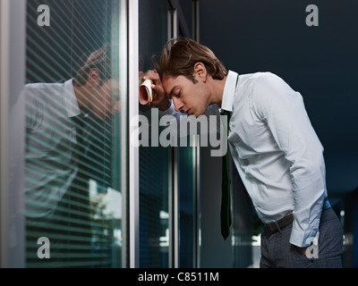 Giovane adulto italiano business man sbattendo la testa contro una finestra in ufficio. Sagoma orizzontale, spazio di copia Foto Stock