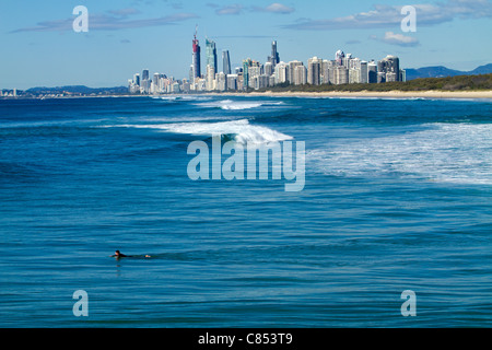 Un surfista paddling verso un'onda con Surfers Paradise in background. Foto Stock