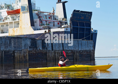 Donna kayak passato dock e nave cargo in attesa di essere caricato con grano nel porto di Churchill in Churchill, MB, Canada. Foto Stock