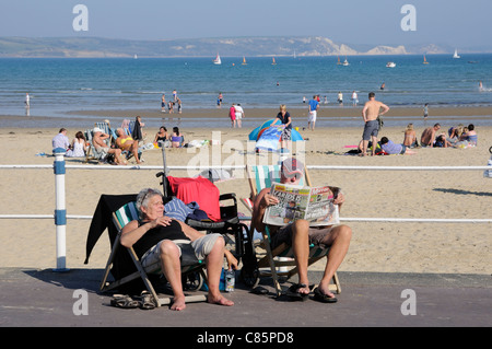 Anziani vacanzieri seduti in sedie a sdraio nella località balneare di Weymouth Dorset England Regno Unito Foto Stock