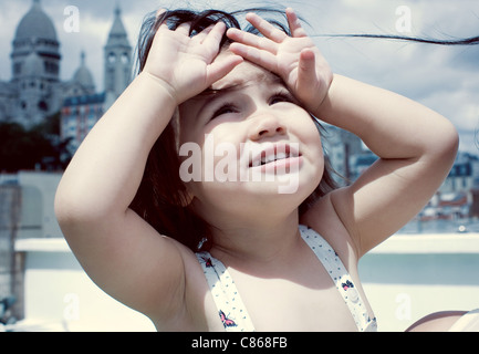 Bambina guardando in alto le mani e gli occhi di ombreggiatura Foto Stock