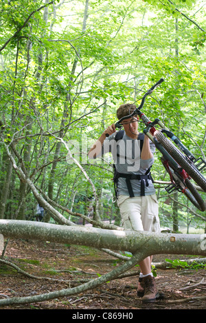 Uomo che porta in mountain bike nei boschi con tronchi di alberi caduti Foto Stock