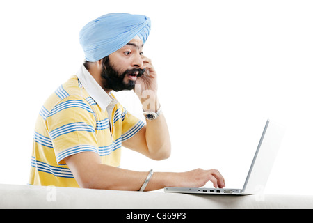 La religione Sikh l uomo a parlare al telefono mentre si lavora su un computer portatile Foto Stock