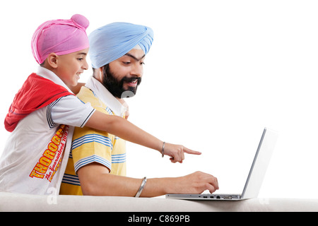 La religione sikh ragazzo puntando verso i suoi padri laptop Foto Stock