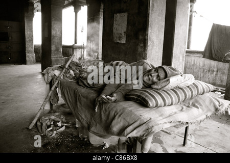 Una donna morente giace su un letto in un edificio abbandonato, Varanasi, India Foto Stock