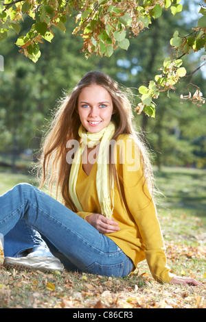 Foto di felice ragazza seduti sulla massa nel parco in autunno Foto Stock