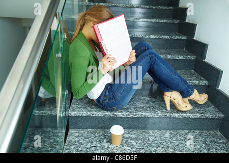 Foto di pretty studente nasconde il suo volto dietro la carta sulle scale del college Foto Stock