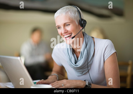 Donna anziana in cuffia utilizzando laptop Foto Stock