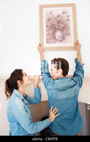 Giovane appendere foto nella nuova casa Foto Stock
