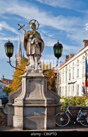 Statua di San Giovanni di Nepomuk, Sint-Jan Nepomucenus, su Wollestraat ponte in Bruges. Torre della chiesa di Nostra Signora in background. Foto Stock