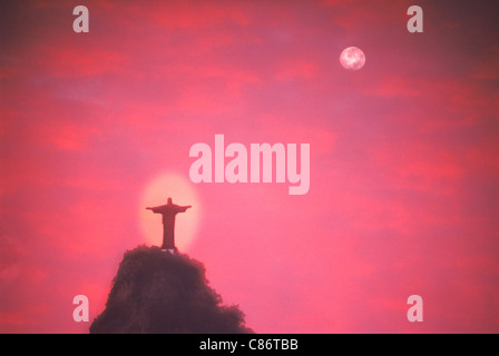 Il Cristo del Corcovado cercando su Rio de Janeiro sotto la luna piena e passaggio di nuvole al tramonto Foto Stock