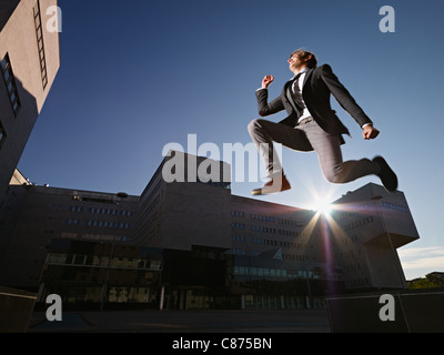 Businessman jumping vicino a edifici per uffici Foto Stock