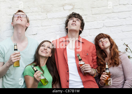 Germania, Berlino, giovani uomini e donne tenendo le bottiglie di birra e guardando in alto, sorridente Foto Stock