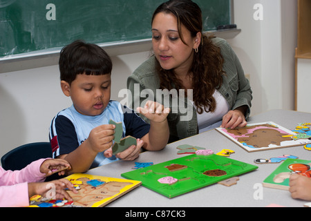 Insegnante di età prescolare aiutando 4 anno agli studenti di mettere insieme un puzzle in aula Foto Stock