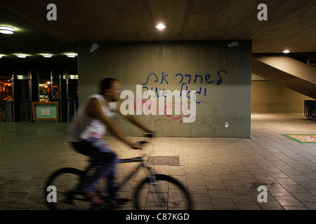 Un bicycler passano da un graffiti in ebraico spruzzata in una parete in corrispondenza del sito in cui Yitzhak Rabin è stato assassinato legge 'Free Yigal Amir,' di Tel Aviv in Israele. "Prezzo" viene utilizzato in riferimento ad atti di violenza politica condotta da destra israeliani protestando governo Israeliano la politica in materia di insediamenti e i palestinesi. Foto Stock