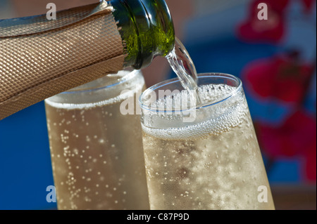 Champagne spumante versando all'aperto closeup bicchieri di vino fresco sulla terrazza soleggiata con fiori Bougainvillea e piscina sullo sfondo Foto Stock