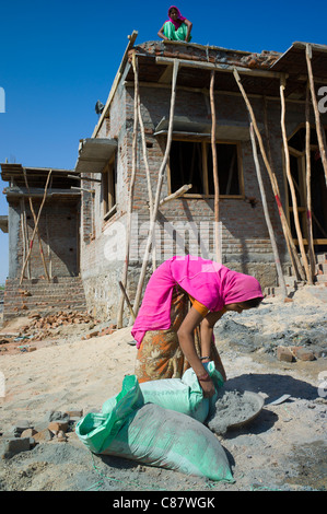 Donna indiana in sari mescolare cemento mentre si lavora sul sito in costruzione al villaggio Khore nel Rajasthan, India settentrionale Foto Stock