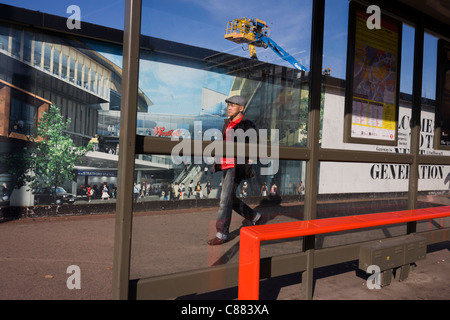 Uomo locale passa una palizzata che mostra l'aspirazione e il consumismo della vicina città di Westfield Shopping Complex, Stratford Foto Stock