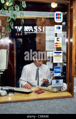 Budapest, Ungheria. Valuta Exhange luogo; donna che guarda ad una carta bancaria seduto dietro la finestra; computer sulla scrivania. Foto Stock