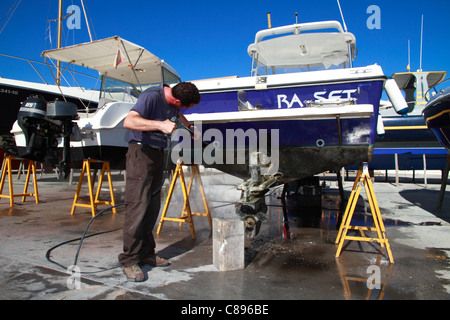 Pulizia marinaio la sua barca scafo con acqua ad alta pressione pistola Foto Stock