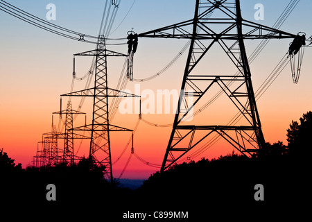 Elettricità tralicci stagliano contro un tramonto Foto Stock