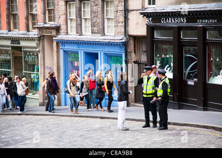 Edimburgo, Scozia, situato nella zona di Grassmarket tortuosa via con la sistemazione di negozi sulla strada basolata traffico operai parlando Foto Stock