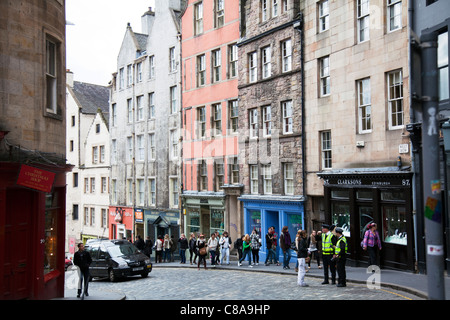 Edimburgo, Scozia, situato nella zona di Grassmarket tortuosa via con la sistemazione di negozi sulla strada basolata traffico operai parlando Foto Stock